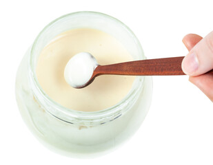 top view of little wooden spoon with natural organic white honey over glass jar with honey isolated on white background