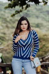 Beautiful model posing for photos on the street. Wearing a blue blouse with white stripes, jeans and a purse.