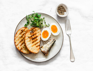 Grilled bread, canned sardines, boiled eggs, micro greens on a light background, top view. Delicious breakfast, snack, tapas