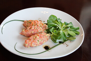 
Two salmon cutlets in caviar on a white plate with a lettuce shot from the top side view.