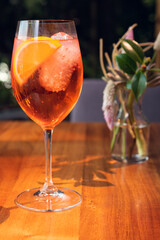 Orange cocktail with orange garnish in wine glass, aperol spritz in sunny setting.