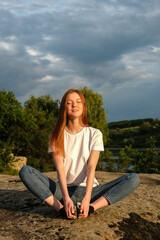 Relaxation, meditation mental health concept. National Relaxation Day. Red-haired woman meditates and relaxes in nature outdoor rocks