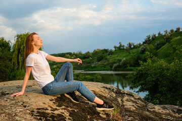Naklejka na ściany i meble Relaxation, meditation mental health concept. National Relaxation Day. Red-haired woman meditates and relaxes in nature outdoor rocks