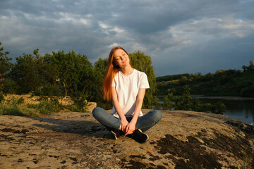 Relaxation, meditation mental health concept. National Relaxation Day. Red-haired woman meditates and relaxes in nature outdoor rocks