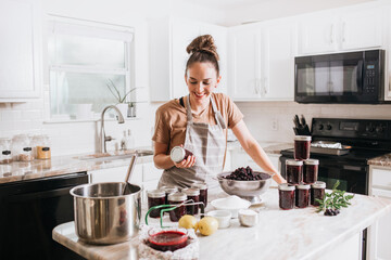 Woman canning homemade blackberry jam in home kitchen