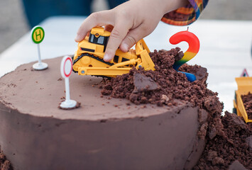 Birthday chocolate cake with bulldozer toy and children hand