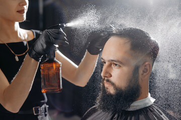 Woman barber cutting hair to a bearded man.