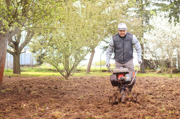 Old man plows the ground with a motor cultivator. A farmer ploughs the soil using a petrol cultivator.