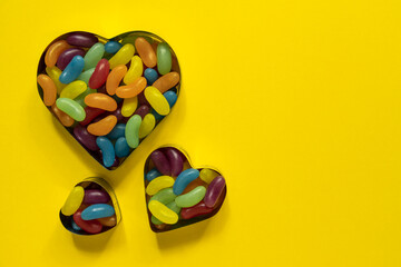 Multi-colored glazed jelly beans sweets in heart cookies molds on yellow backgrouns with copy space.