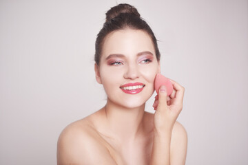 Beautiful portrait of a girl who touches her skin. Brunette with a delicate pink make-up, applies the cream with a sponge. Makeup brushes, foundation. Beauty egg