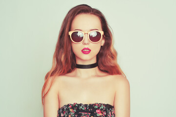 A girl in sunglasses and with long hair is looking directly at the camera. Model in a choker with big red lips in wooden glasses. Fashion