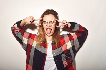 Beautiful fashionable girl makes faces, laughs, has fun, glasses for vision a plaid shirt Shows language
