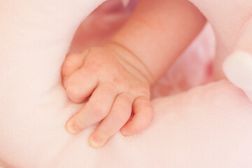 Fototapeta na wymiar Mão de bebê em close up segurando uma mantinha rosa fofa. Detalhes do braço de um recém nascido com um paninho.
