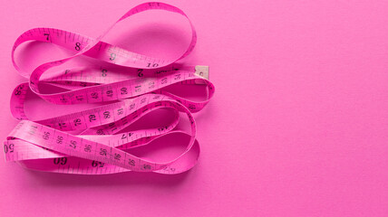 Pink centimeter on pink background. Simple flat lay with pastel texture. Fitness concept. Stock photo.
