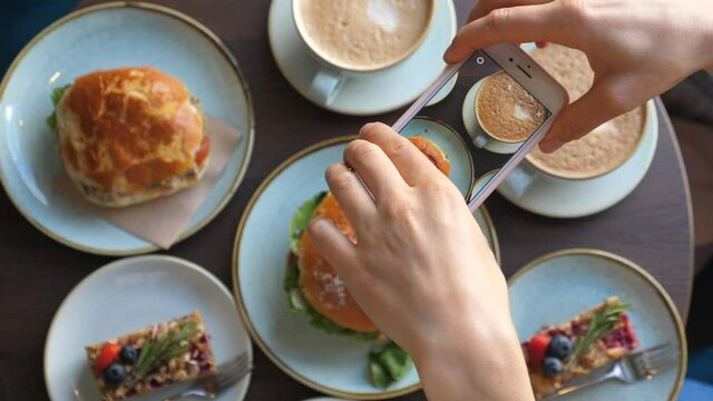 Woman Taking Overhead Photo Of Food In Cafe Using Smartphone During Breakfast