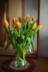 Bouquet of red-yellow tulips in glass vase in front of a mirror, home decor, still life, selective focus