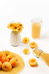 Apricots, a vase with flowers, a glass and a bottle with apricot juice isolated on a white background.