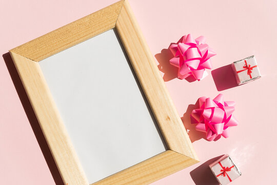 Mock-up of wooden frame with copy space for poster and gift boxes, pink satin bow on pink background.Mother's Day, Women's Day or other suitable holiday card, photo frame with copy space for text