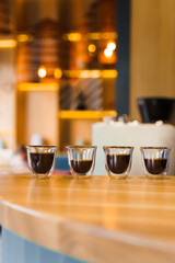 4 Flavored coffee espresso in double glass cup with sun light on background in cafe. Coffee on the wooden table with blurred background. Vertical photo for advert in social networks.