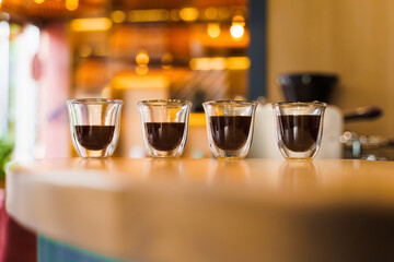 4 Flavored coffee espresso in double glass cup with sun light on background in cafe. Coffee on the wooden table with blurred background