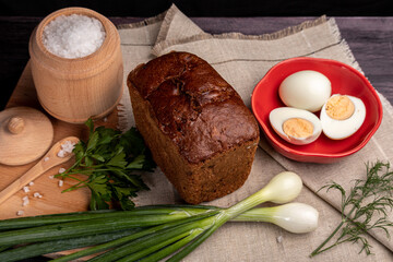 black bread on a linen napkin with green onions, eggs and salt in a wooden jar
