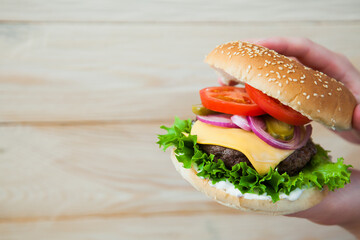 Hands holding homemade beef burger on wooden table. Ready to eat tasty fast food hamberger. Unhealthy food concept.