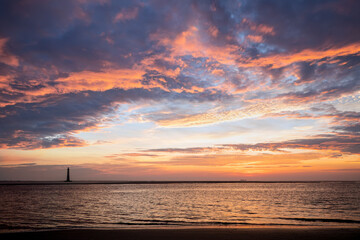 Photographed from Folly Island, the historic Morris Island Lighthouse and a ship on the horizon are silhouetted by a colorful sunrise sky over the Atlantic Ocean near Charleston, South Carolina.