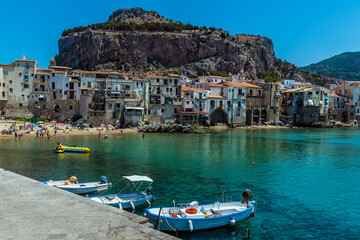 Fototapeta na wymiar Small boats moored against the harbour walls of Cefalu, Sicily with the town and the Mesa as a backdrop it in summer