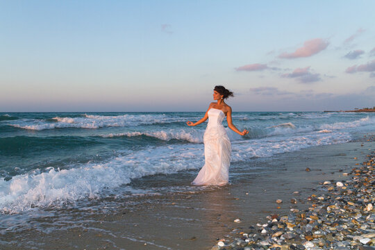 Young beutiful bride feeling free and happy, breathing clean fresh ocean air on a sandy beach in summer at dusk.