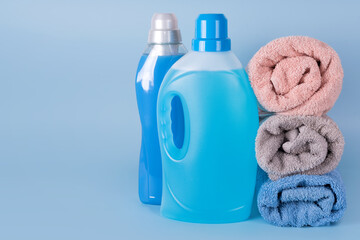 Obraz na płótnie Canvas Bottles of detergent and fabric softener with clean towels on blue background. Containers of cleaning products, household chemicals. Liquid detergent and conditioner. Laundry day, cleaning concept.