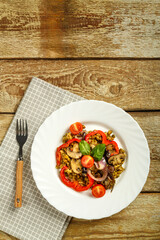 On a wooden table is a white plate masha with vegetables and mushrooms on a napkin and a fork. Copy space.
