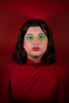 Modelo con maquillaje verde y pelo casta&ntilde;o mirando a c&aacute;mara con fondo y remera roja  