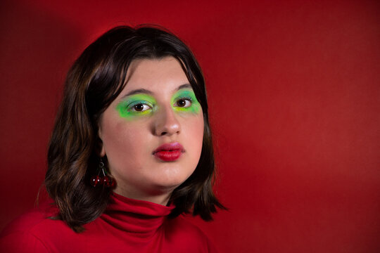 Modelo con maquillaje verde y pelo casta&ntilde;o mirando a c&aacute;mara con fondo y remera roja  