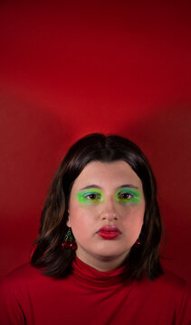Modelo con maquillaje verde y pelo casta&ntilde;o mirando a c&aacute;mara con fondo y remera roja  