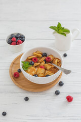 Bowl for breakfast with tiny pancake cereal with blueberries, raspberries, mint