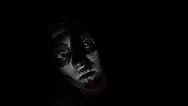 Girl with traditional Santa Muerte makeup smiles in the strobe light. Theme of costumes and transformation for holiday of Halloween. Standard skull makeup for the day of the dead celebration