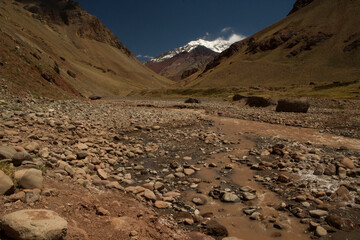 Seven summits. Rocky stream flowing downhill along the valley. Mountain Aconcagua, highest peak in America, in the background.