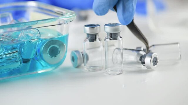 hand of scientist doctor use plier or tweezer holding ampoule bottle to clean in blue alcohol on glassware at hospital lab. Researcher in laboratory Try to extract the vaccine for coronavirus covid19 