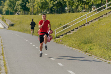 Male athlete wearing a red t-shirt is running with a parachute in the park