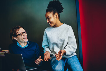 Diversity male and female colleagues cooperating on making online research using laptop computer indoors multiracial family looking at each other having conversation at home interior using netbook