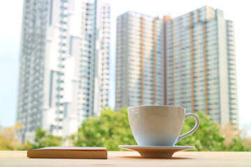 Cup of coffee with a book against blurry modern high buildings in the backdrop