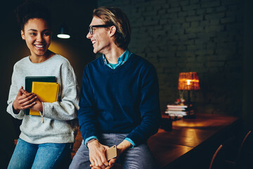 Smiling multiracial male and female colleagues talking to each other and having fun during communication on break, positive hipsters students enjoying break and conversation on free time indoors.