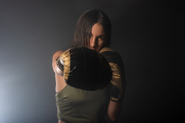 Close up dark portrait of a young and sexy female boxer punching direct hit with boxing gloves