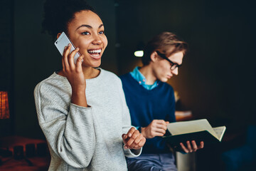 Cheerful young african american woman excites with getting good news during telephone conversation while her male colleague read report in office, smiling female satisfied with operator consultancy