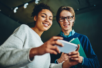 Portrait of cheerful multiracial woman and man looking at camera while using 4G connection on smartphone for browsing, happy hipster girl and guy using mobile phone for networking on free time.
