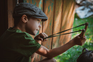 young boy with slingshot shooting - obrazy, fototapety, plakaty