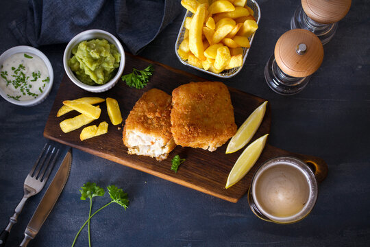 Battered fish with french fries, mushy peas and sauce. Fish and chips, glass of beer. Overhead horizontal image