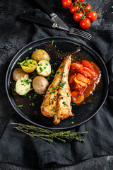 Baked in tomatoes monkfish with potatoes and vegetables. Black background. Top view