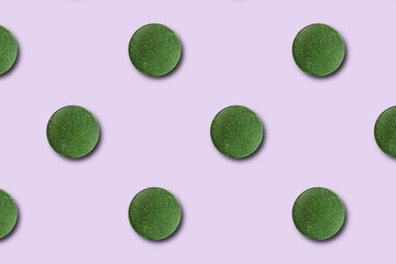 Seamless pattern of green chlorella or spirulina tablets on a pink background.