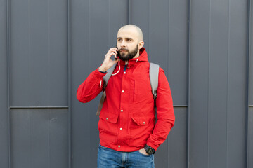 Portrait of a brutal guy with a beard in casual clothes who is talking on the phone on the street